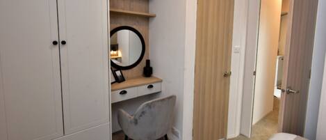 A bedroom with a bed, a desk with a chair, a wardrobe, and a door leading to another room.