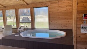 A wooden cabin with a hot tub, large windows, and a picnic table outside.