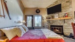 A cozy room with a fireplace, a bed with a red blanket, and a large window with a view of trees.