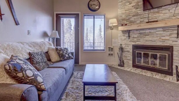 A cozy living room with a sofa, a coffee table, a fireplace, and a clock on the wall.