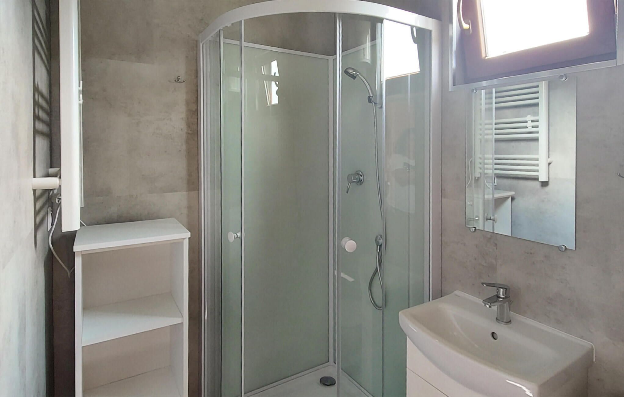 Un bany amb plat de dutxa tancat per vidre, un lavabo blanc i un mirall a sobre.