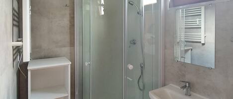 A bathroom with a glass-enclosed shower, a white sink, and a mirror above it.