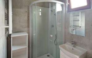 Un bagno con cabina doccia in vetro, un lavandino bianco e uno specchio sopra.