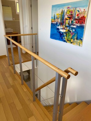 A staircase with a wooden handrail and metal balusters, leading to a landing with a white wall and a colorful painting.