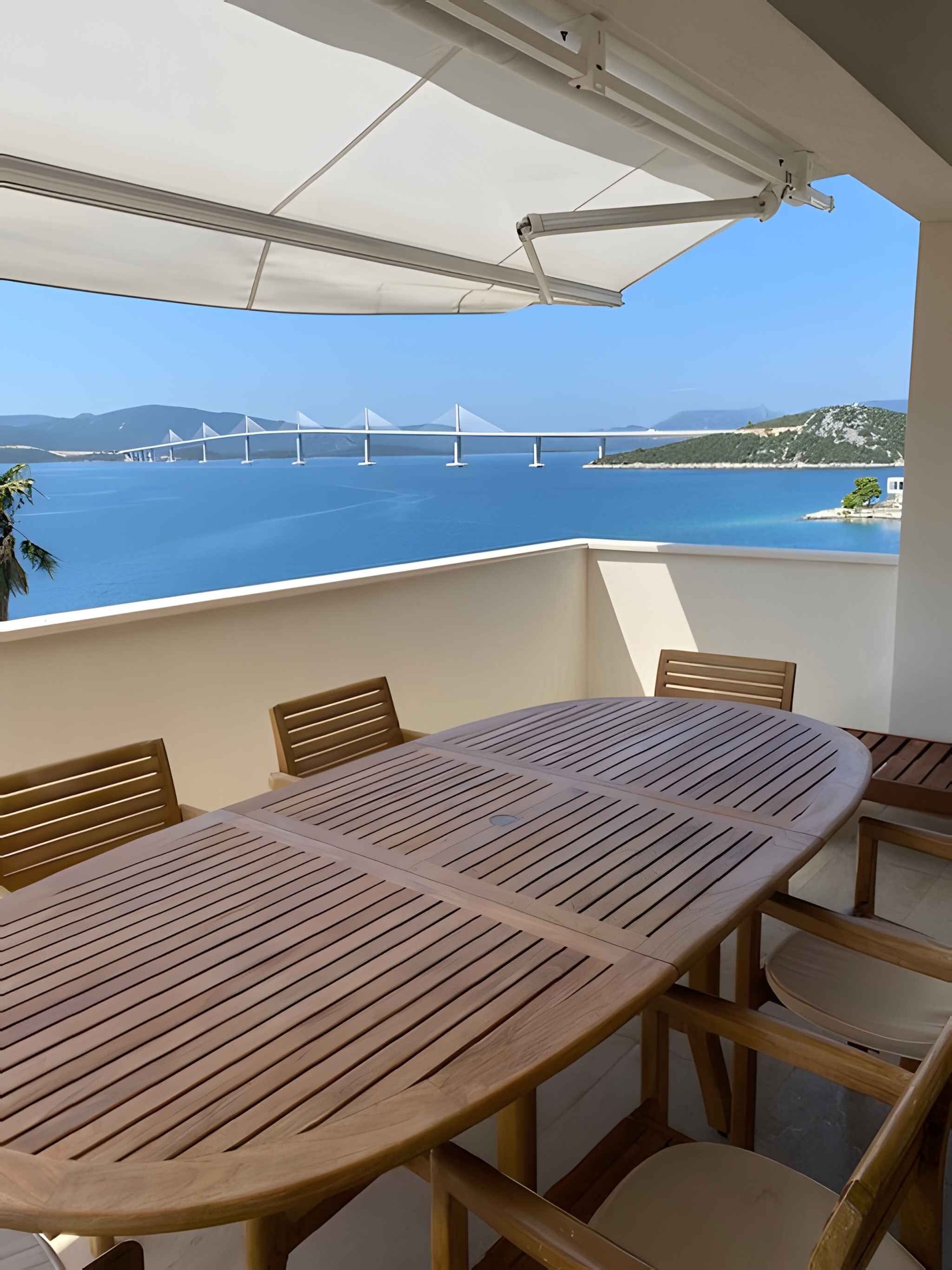 Ein Balkon mit Tisch und Stühlen, mit Blick auf ein Gewässer und eine Brücke.