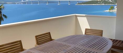 A balcony with a table and chairs, overlooking a body of water and a bridge.