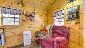 Ein gemütliches Blockhaus-Interieur mit Holzwänden, einem roten Sofa, einem Fenster mit Vorhängen und einem Willkommensschild.