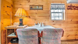 Ein gemütliches Blockhauss-Interieur mit Holzwänden, einem Tisch mit Stühlen, einer Lampe, einem Fenster mit Vorhängen und einer Wanddekoration.
