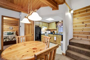 Ein gemütliches Interieur im Blockhausstil mit einem Holzesstisch, Stühlen, einer Küche mit Holdekor, einem Kühlschrank und einer Treppe.