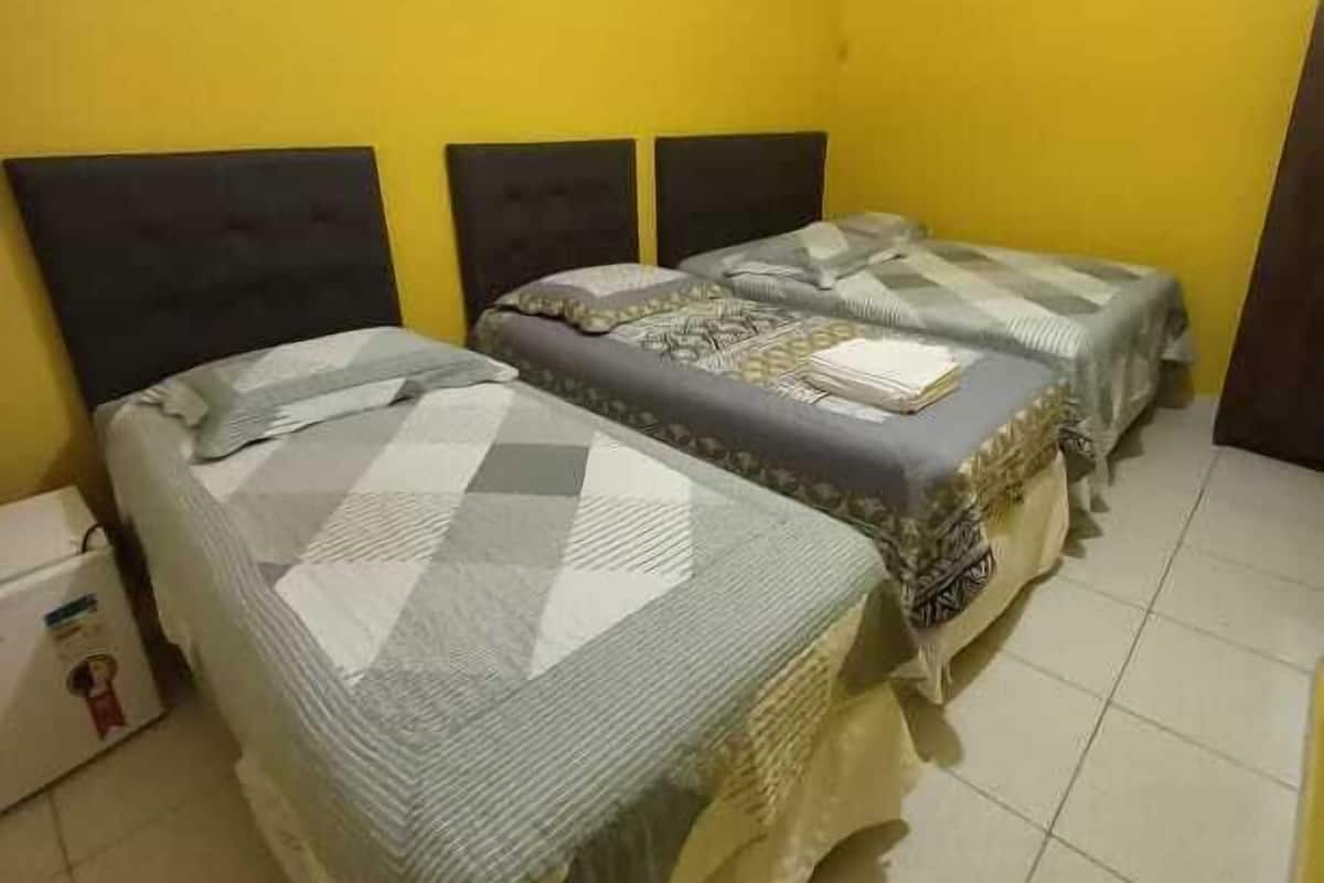 A room with two beds, each with a headboard and a patterned bedspread. The walls are painted yellow, and the floor is tiled.