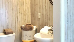 A bathroom with a wooden wall, a white toilet, a white sink, and a wooden stool with towels.