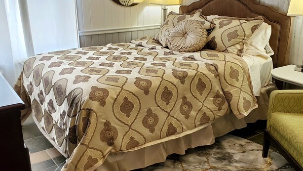 A bed with a patterned bedspread, two bedside lamps, a round mirror, and a marble-patterned rug.