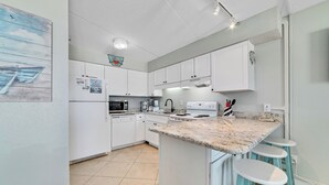 Een moderne keuken met witte kasten, een granieten aanrechtblad en een inbouw-kookeiland met barstoelen.
