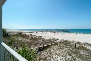 A beach with a wooden pier extending into the ocean, a sandy beach, and a grassy area with a wooden walkway. - Emerald Skye 13 - Cozy, Cute Beachy Decor, GREAT View & Outdoor Heated Pool (Orange Beach)