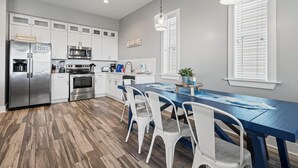 Una cucina moderna con mobili bianchi, elettrodomestici in acciaio inossidabile e un tavolo da pranzo blu con sedie bianche.