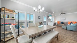A modern living room with a wooden dining table, cushioned chairs, a sofa, and a TV. - Attitude Adjustment-CONVENIIENT LOCATION, PRIVATE POOL, GREAT FOR FAMILIES! (Gulf Shores)
