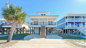 A beachfront property with a central staircase leading to a two-story building, a palm tree, and a clear blue sky. - Attitude Adjustment-CONVENIIENT LOCATION, PRIVATE POOL, GREAT FOR FAMILIES! (Gulf Shores)