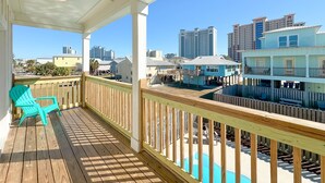A wooden deck with a pool, a turquoise chair, and a view of nearby buildings. - Attitude Adjustment-CONVENIIENT LOCATION, PRIVATE POOL, GREAT FOR FAMILIES! (Gulf Shores)