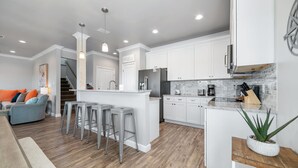 A modern kitchen with white cabinets, stainless steel appliances, and a central island with bar stools. - Attitude Adjustment-CONVENIIENT LOCATION, PRIVATE POOL, GREAT FOR FAMILIES! (Gulf Shores)