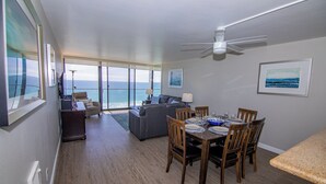 A spacious living area with a dining table set for six, a ceiling fan, and a view of the ocean through large windows. - ONE BEDROOM CONDO 402 FULL BEACH AND OCEAN VIEW (San Diego)