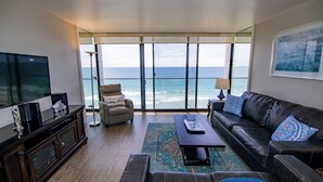 A living room with a large TV, leather sofa, and a view of the ocean through floor-to-ceiling windows. - ONE BEDROOM CONDO 402 FULL BEACH AND OCEAN VIEW (San Diego)