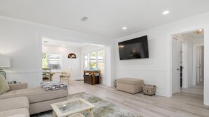 Un salon avec un canapé beige, une table basse en verre, un téléviseur fixé au mur et un plancher en bois.