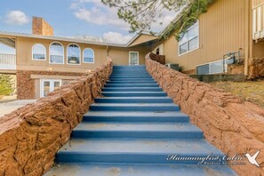 A staircase leading to a house with a stone wall on one side and a wooden exterior on the other. - Big Bear with game room! Sleeps 18. (Ruidoso)