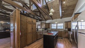 A spacious kitchen with wooden cabinets, a central island, and a stone fireplace. - Big Bear with game room! Sleeps 18. (Ruidoso)