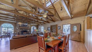 A spacious living area with a fireplace, wooden ceiling beams, and a dining table set for four. - Big Bear with game room! Sleeps 18. (Ruidoso)