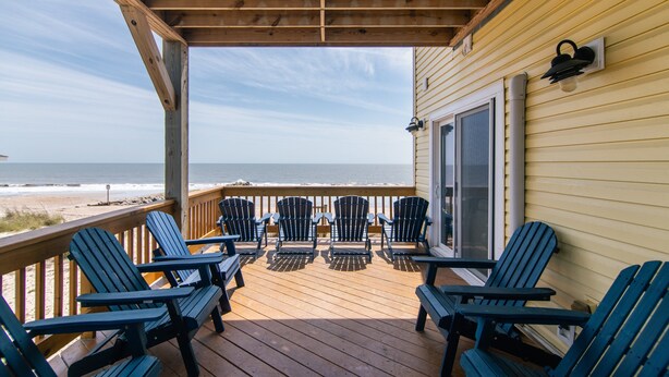 A wooden deck with chairs and a table, overlooking a beach.