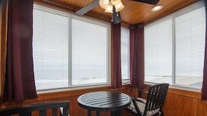 A room with wooden paneled walls, a round table with a chair, and large windows with blinds.