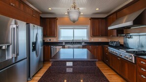 A modern kitchen with stainless steel appliances, a large island, wooden cabinets, and a window above the sink.