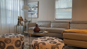 A living room with a sofa, ottomans, a coffee table, a lamp, and a painting on the wall. - Entire House - 5 Minutes Drive to AT&T Stadium (Arlington)