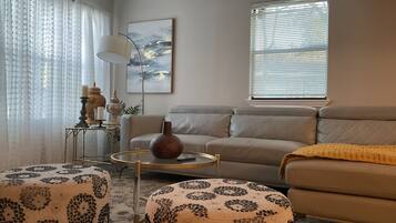 Un salon comprenant un canapé, des poufs, une table basse, une lampe et un tableau accroché au mur.
