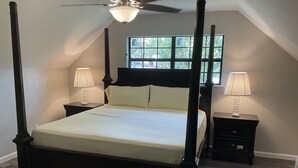 A four-poster bed with a headboard, two bedside tables, and a window with a view of trees. - Entire House - 5 Minutes Drive to AT&T Stadium (Arlington)