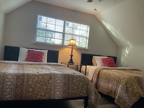 Une chambre avec deux lits, une fenêtre avec des stores, une lampe de table et un ventilateur de plafond.