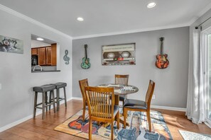 Un coin repas avec une table ronde, quatre chaises, une cuisine en arrière-plan et des guitares accrochées au mur.