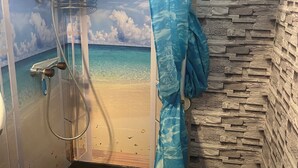 Een badkamer met een douche, een wastafel en een wand met een stenen textuur.