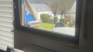Een kamer met raam dat uitkijkt op een woonwijk, een bed en een radiator.