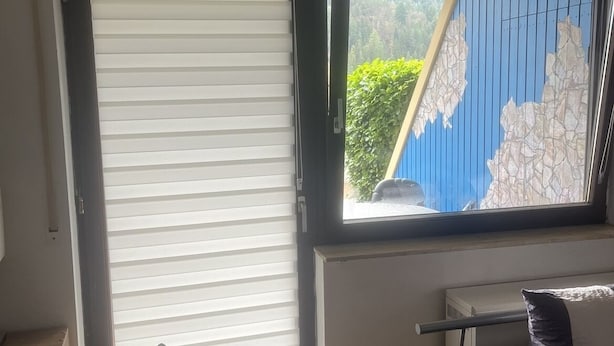 Een kamer met een grote schuifdeur, een raam met uitzicht op groen, een bed en een klein tafeltje met een kussen.