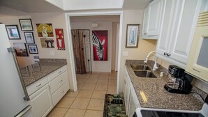 A compact kitchen with granite countertops, a coffee maker, and a microwave. There are framed pictures on the walls and a door with a zebra design. - ONE BEDROOM CONDO 809 (San Diego)