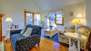 Ein gemütliches Wohnzimmer mit einem blauen, floralen Sofa, einem gelben, floralen Sessel, einem weißen Couchtisch und Holzboden.