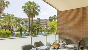 Un balcon avec une table dressée pour deux personnes, offrant une vue sur des palmiers et une piscine.