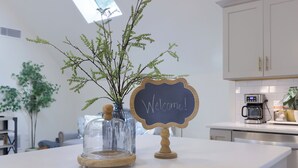 Una encimera de cocina con una cloche de vidrio transparente sobre una planta, un cartel de bienvenida y una cafetera.