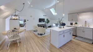 Una cocina moderna con armarios blancos, una isla central y una zona de comedor con mesa y sillas de madera.