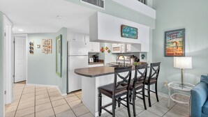 A modern kitchen with a central island, white cabinetry, and a dining area with chairs.