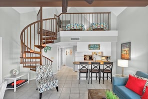 A spacious living area with a wooden spiral staircase, a kitchen with a central island, and a dining area with a blue sofa and red cushions. - Gulf Shores Plantation-West 1353 (Gulf Shores)