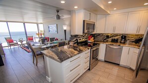 A modern kitchen with white cabinets, a granite countertop, stainless steel appliances, and a dining area with a view. - TWO BEDROOM CONDO 708 (San Diego)