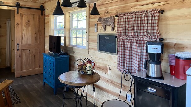 A wooden cabin interior with a blue dresser, a round wooden table, a Bunn coffee maker, and a chalkboard menu. - Brand new tiny cabin located on farm. Near rivers, trailsheads & national forest (West Plains)