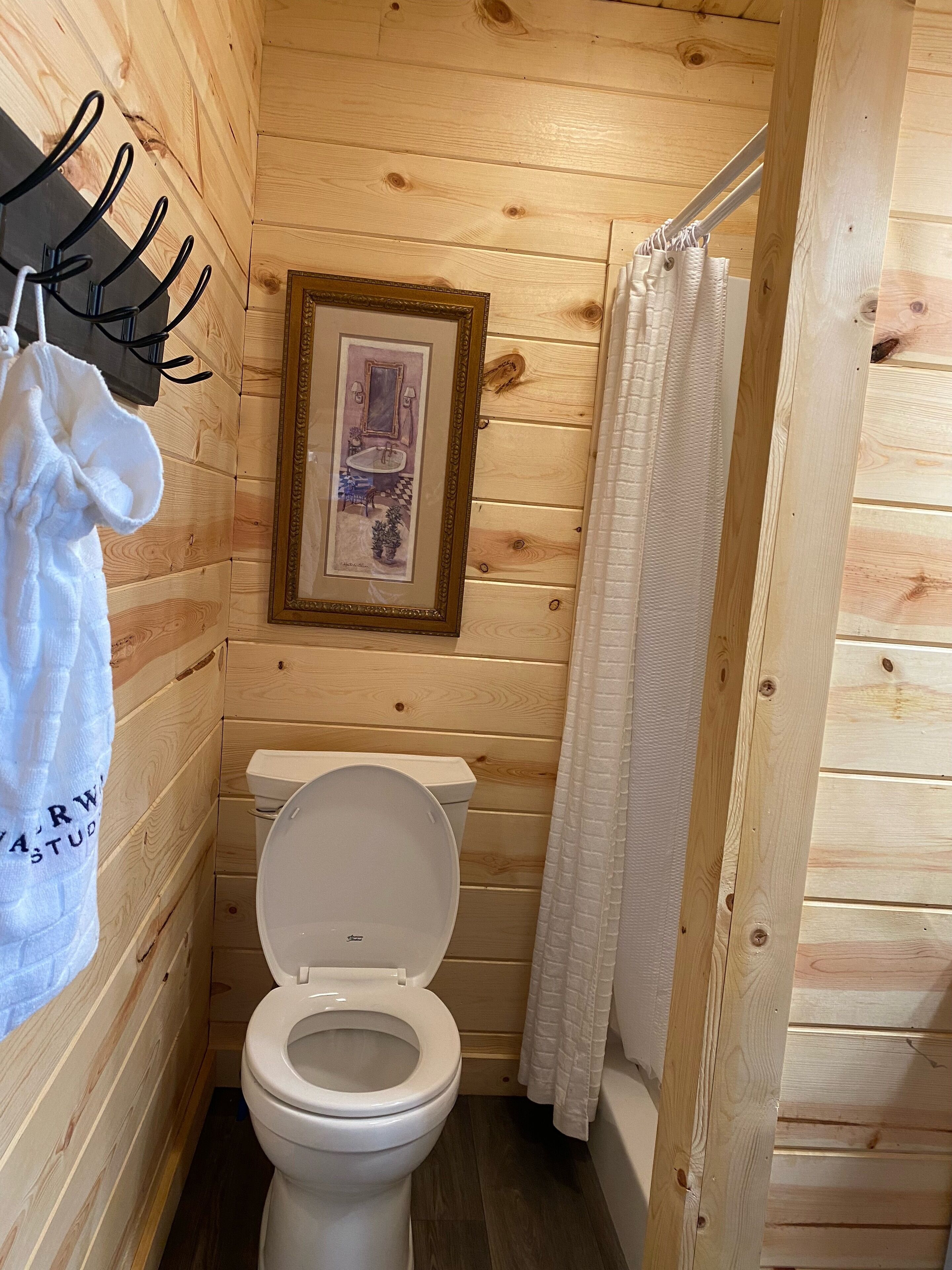 A wooden-paneled bathroom with a toilet, a framed picture on the wall, and a towel hanging on a hook.